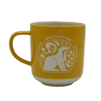 A yellow stoneware mug with 'Hufflepuff' text and a badger design, along with the house's values: Patience, Dedication, Loyalty.