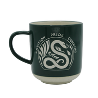 A deep emerald green stoneware mug with white text and a white base featuring a white serpent design and traits associated with the Slytherin house from the Harry Potter series.