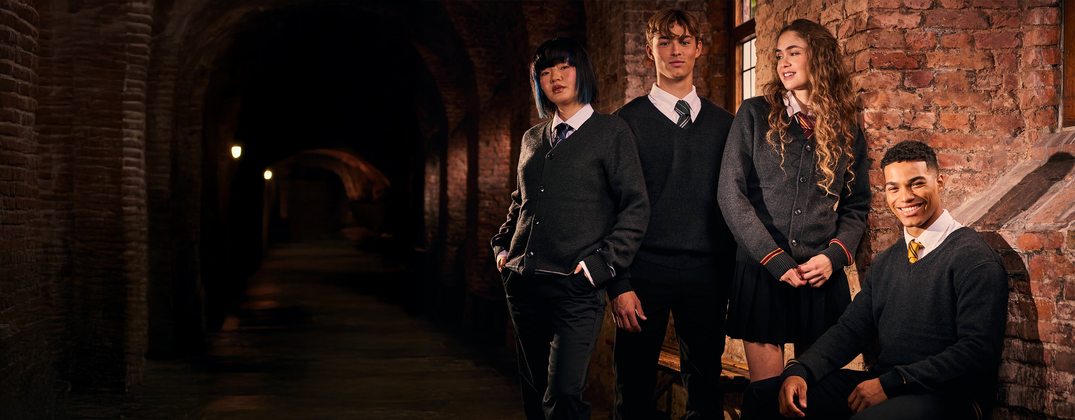 Four individuals in formal Hogwarts attire standing in a dimly lit hallway with brick walls.
